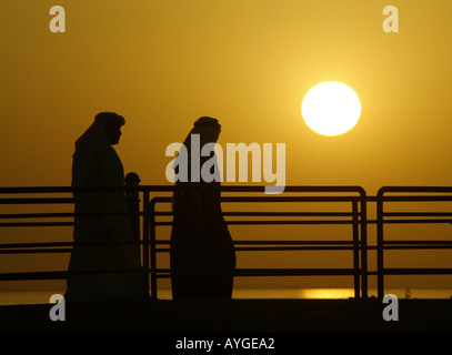 Kuwaitis in traditioneller Kleidung spazieren das Dock an der Uferpromenade der Sonnenuntergang über dem Persischen Golf Stockfoto