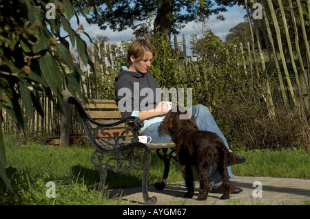 Frau trinkt Tee sitzen auf Bank mit Hund zu ihren Füßen Stockfoto