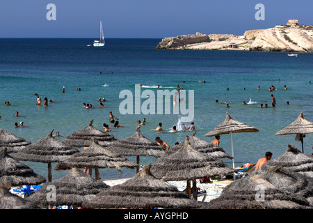 Strohgedeckte Sonnenschirme säumen Monastir Strand wo Urlauber Abkühlung im Wasser Tunesien Stockfoto