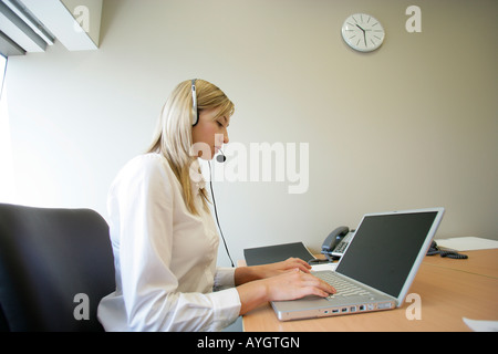 Geschäftsfrau trägt Kopfhörer und arbeiten mit Laptop im Büro Stockfoto