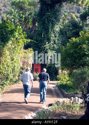 Männer gehen auf schattigen Weg in eine rote Telefonzelle in Alameda Botanische Gärten, Gibraltar, Stockfoto