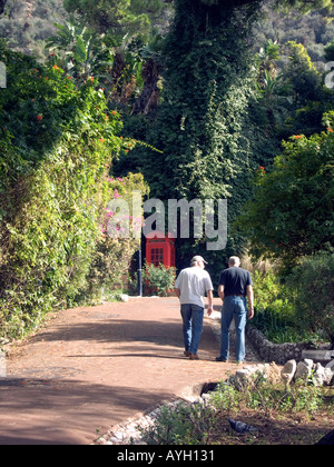 Männer gehen auf schattigen Weg in eine rote Telefonzelle in Alameda Botanische Gärten, Gibraltar, Stockfoto