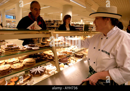 Verkäuferin in Uniform und Hut auf der Patisserie-Zähler bei Waitrose, Großbritanniens führende Qualität Supermarkt Stockfoto