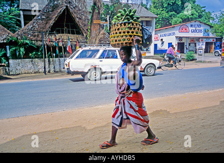 Afrika Kenia MALINDI kenianische Frau gekleidet in traditionellen Kanga Tuch stillen ihr Baby während des Tragens von Bananen in den Markt ein Stockfoto