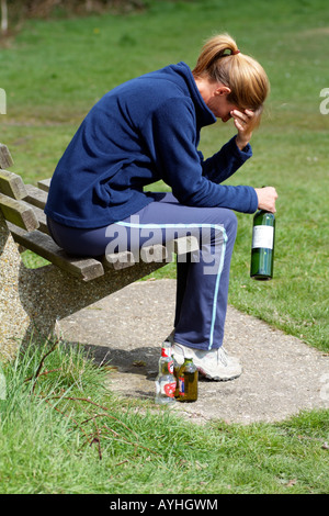 Frau mit einem Alkoholproblem sitzt auf der Parkbank mit Wein- und Bierflaschen Stockfoto