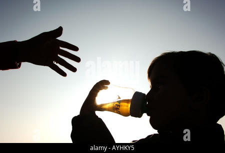 Kleinkind aus Flasche trinken, während die Hand des übergeordneten streckt Stockfoto