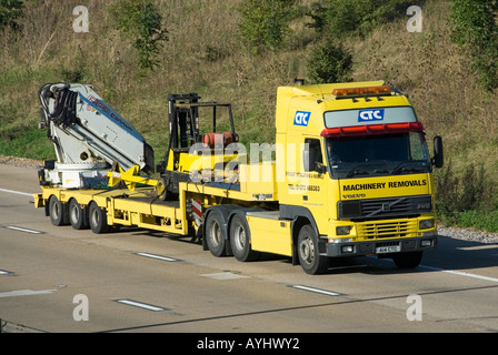 M25-Autobahn-Seitenansicht knickgelenkter Tieflader-Anhänger mit schweren Maschinen hinter gelbem Volvo-Lkw London Orbital Road Essex England Großbritannien Stockfoto