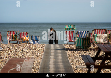 Paar am Strand mit Blick auf Meer, umarmt.  Sie sind umgeben von bunten Liegestühlen. Stockfoto