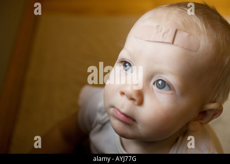 Ein Kleinkind mit einem Verband auf dem Kopf in natürlichem Licht. Stockfoto