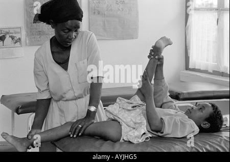 S/W einer Physiotherapeutin, die die Beine eines jungen Jungen manipuliert, der Opfer von Polio ist, in einer Klinik in Asele, Shoa, Äthiopien, Afrika Stockfoto