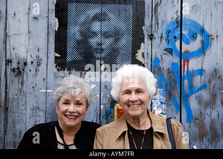 Zwei attraktive Frauen in Führungspositionen lächelnd vor einer Wand von Graffiti. Stockfoto