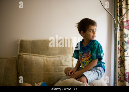 Jungen im Alter von sechs Jahren am Arm des Sofas sitzt und schaut aus Fenster Stockfoto