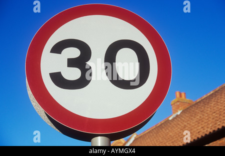 Nahaufnahme eines kreisförmigen Tempolimit Schild besagt 30 gegen blauen Himmel mit orange Ziegel und Fliesen Haus hinter Stockfoto