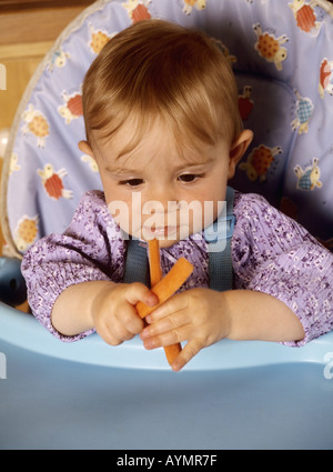 Babymädchen sitzen in einem Hochstuhl Blick auf frische Karotten Stockfoto