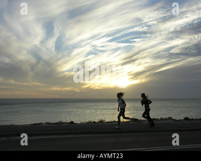 Zwei junge Frauen, die entlang Meer bei Sonnenuntergang Stockfoto