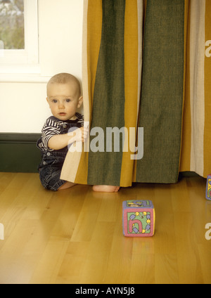 Baby Boy peering aus Vorhänge Stockfoto