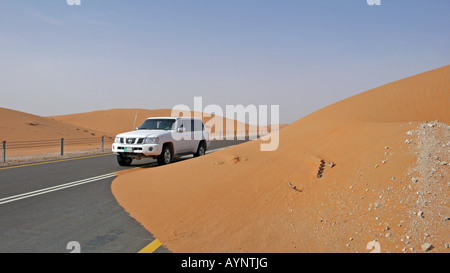 Ein Nissan Patrol 4x4 passiert einen Sandfall auf einer abgedichteten Straße in der Liwa Oasis, Western Region, Abu Dhabi Emirat, VAE. Stockfoto