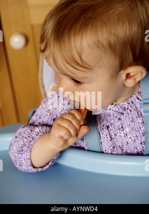 Babymädchen sitzen in einem Hochstuhl Essen eine Karotte Stockfoto