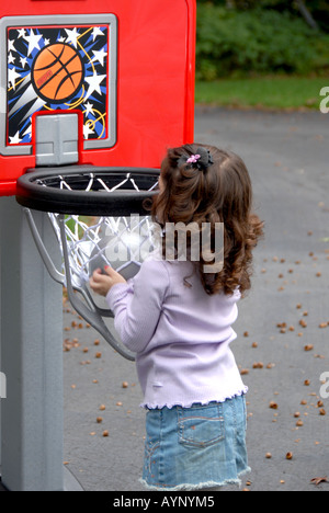 Drei Jahre altes Mädchen beobachten einen Basketball fallen durch den Reifen Stockfoto