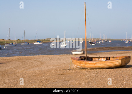 Segelboot aus Holz Klinker gebaut auf Sand mit Booten und Yachten auf dem Meer an Brancaster Staithe Norfolk in England Stockfoto