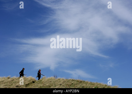 Zwei junge Burschen, die entlang einer grasbewachsenen Bank mit einem blauen Himmel im Hintergrund. Stockfoto