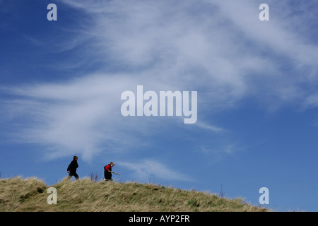 Zwei junge Burschen, die entlang einer grasbewachsenen Bank mit einem blauen Himmel im Hintergrund. Stockfoto