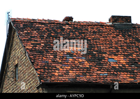 Nahaufnahme eines verwitterten Ziegeldaches auf einem alten Haus in Grodzisk Wielkopolski Polen, das alte Ziegelsteine und Schornsteine vor einem weißen Himmel zeigt. Stockfoto