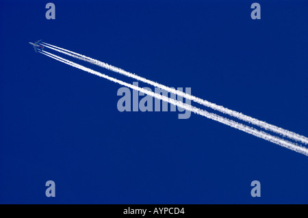 Passagierjet, der in großer Höhe fliegt, hinterlässt lange weiße Kondensstreifen vor einem klaren blauen Himmel. Stockfoto