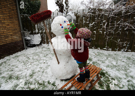 Drei Jahre alten Mädchen, das einen Schneemann in ihrem Garten Stockfoto