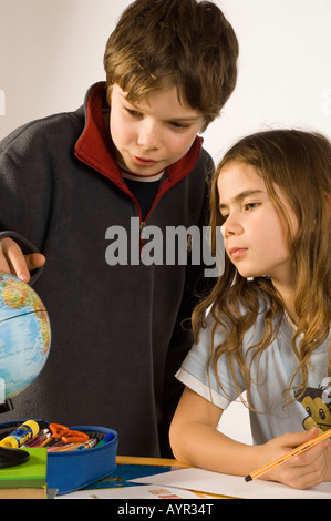 Geschwister, Ten-Year-Old Boy und seine neun-jährige Schwester Hausaufgaben, mit Blick auf einen Globus Stockfoto