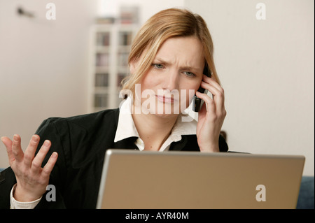 Junge blonde Frau vor Laptop, telefonieren Stockfoto