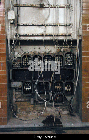 Stark zerstörte Elektroanlagen mit freiliegenden Kabeln und defekten Bauteilen in einem verfallenen Industrieumfeld. Stockfoto