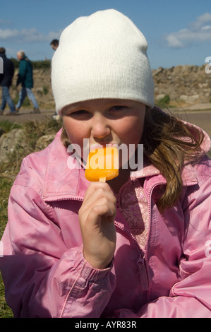 Porträt von netten Mädchen in wolligen Hut essen Eis am Stiel, Lindisfarne, Northumberland, UK Stockfoto