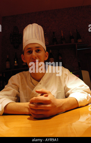 Professioneller Häuptling mit weißem Hut und weißer Jacke, der an einem Tisch in der Küche des Restaurants sitzt. Stockfoto