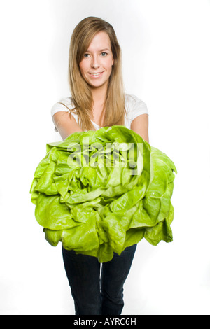 Lächelnde junge Frau mit lange dunkel-Blonde Haare bieten einen großen Kopf grüner Salat Stockfoto