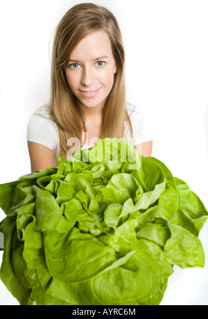 Lächelnde junge langhaarige Frau bietet einen großen Kopf grüner Salat Stockfoto