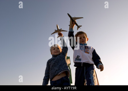 zwei junge Spielzeug Flugzeuge über ihren Köpfen mit klaren Dämmerung Himmel im Hintergrund zu halten Stockfoto