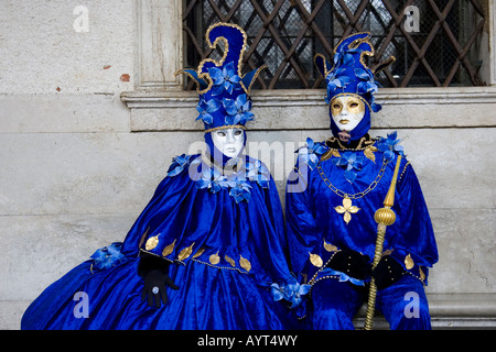 Zwei Personen tragen blaue Kostüme und Masken sitzen auf einer Bank vor einem Fenster, Carnevale di Venezia, Karneval in Venedig Stockfoto