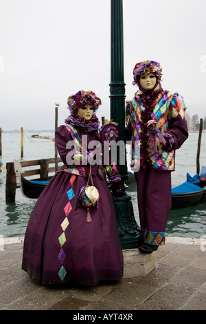 Zwei Personen tragen lila Kostüme und Masken vor Gondeln, Carnevale di Venezia, Karneval in Venedig, Italien Stockfoto