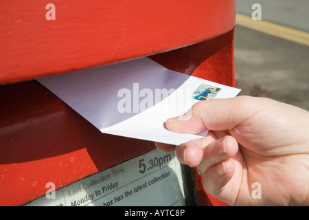 Nahaufnahme der Hand der Person, die die Buchung ein Schreiben mit 2. Klasse Stempel in einen roten Briefkasten zu veröffentlichen. England Großbritannien Stockfoto