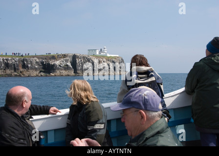 Touristen auf Billy Shiels Boot auf den Farne Islands mit Longstone Leuchtturm im Hintergrund Stockfoto