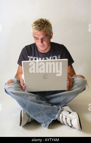 Zwanzig Jahre alten männlichen sitzen gekreuzten Beinen mit einem Apple Mac Laptop. Stockfoto
