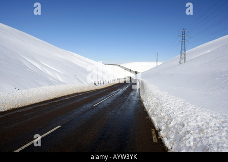 Die A939 Lecht Straßenlauf, von Cockbridge nach Tomintoul, Schottland, mit Schnee auf den umliegenden Hügeln in der Wintersonne Stockfoto