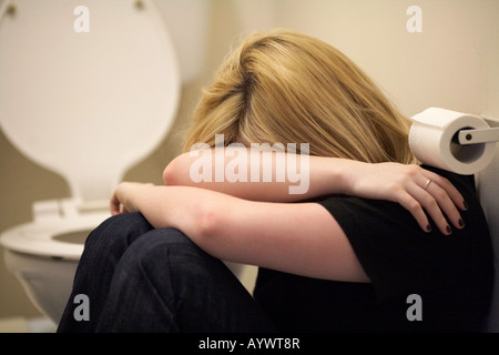 Nahaufnahme der Arme und Schultern der blonde junge Frau sitzt in der fetalen Position auf dem Boden der Toilette Model Released image Stockfoto