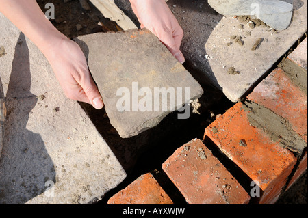 EINE WEIBLICHE BUILDER VERLEGUNG EINER TERRASSE IN EINEM HÄUSCHEN UNTER RENOVIERUNG UK Stockfoto