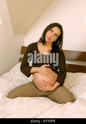 Schwangere Frau auf dem Bett sitzend Stockfoto