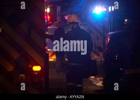 Feuerwehrmann mit Helm und Schutzkleidung tragen insgesamt ein Fall öffnet Tür für ein Feuerwehrauto auf einer Straße bei Nacht Nordirland Feuerwehr Stockfoto