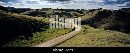 Unter endlosen Himmel bedeckt ein Land Straße Fäden durch leere Rasen Hügel von Theodore Roosevelt Nationalpark North Dakota Stockfoto