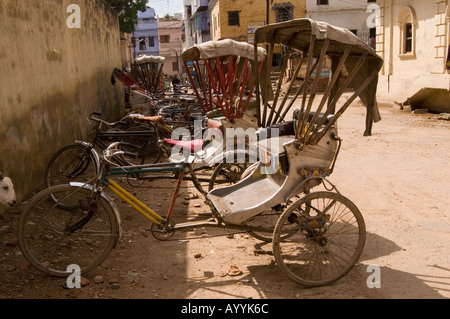 Eine Reihe leerer Radrikschas, die auf einer staubigen Straße in Varanasi, Uttar Pradesh, Indien, geparkt sind. Stockfoto