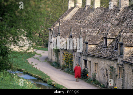 Eine Dame im roten Mantel Spaziergänge Vergangenheit Cotswold Cottage, Bibury, Gloucestershire, England Stockfoto